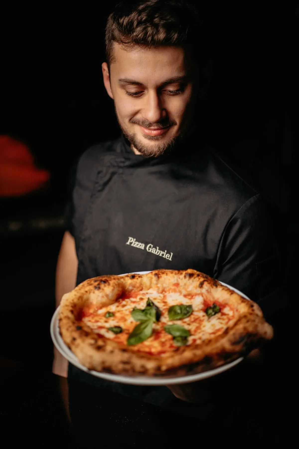 Chef holding a pizza on a plate in a dark kitchen.