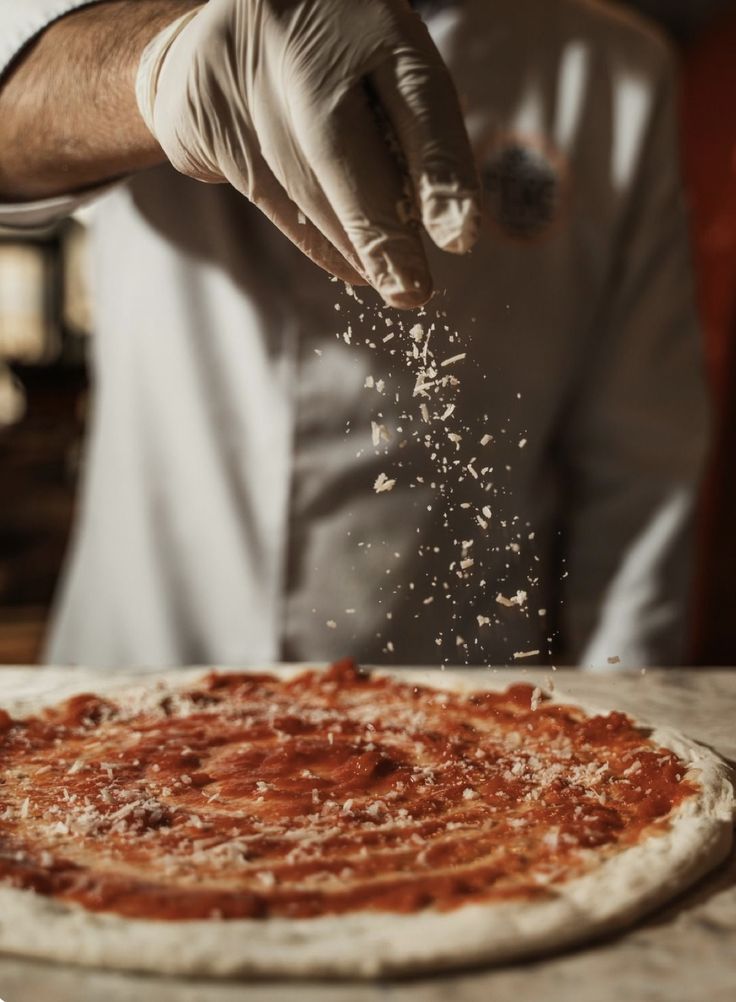 Chef dusting flour over a prepared pizza base.
